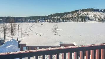 Paisaje nevado con cielo despejado, una terraza de madera y una vista distante de casas en una colina.