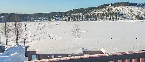 Ett snötäckt landskap med klar himmel, en träveranda och en avlägsen utsikt över hus på en kulle.