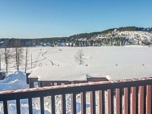 A snow-covered landscape with a clear sky, a wooden deck, and a distant view of houses on a hill. - Skivillas 61 ukkohalla (b1) by Interhome (Hyrynsalmi)