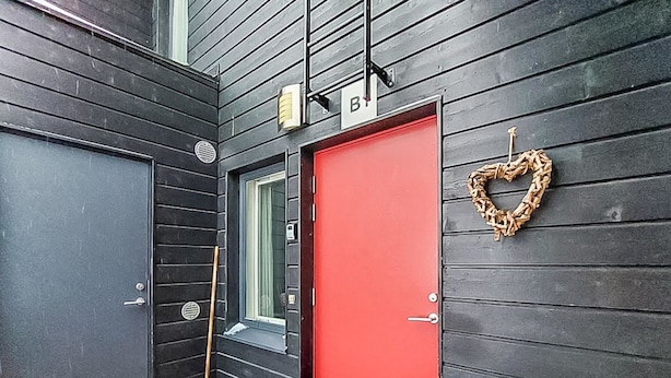 En svart dörr med en röd dörr bredvid, ett litet fönster och en hjärtformad krans på väggen.