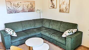 Ein grünes Ecksofa mit zwei Kissen, einem kleinen runden Tisch und einer Stehlampe.
