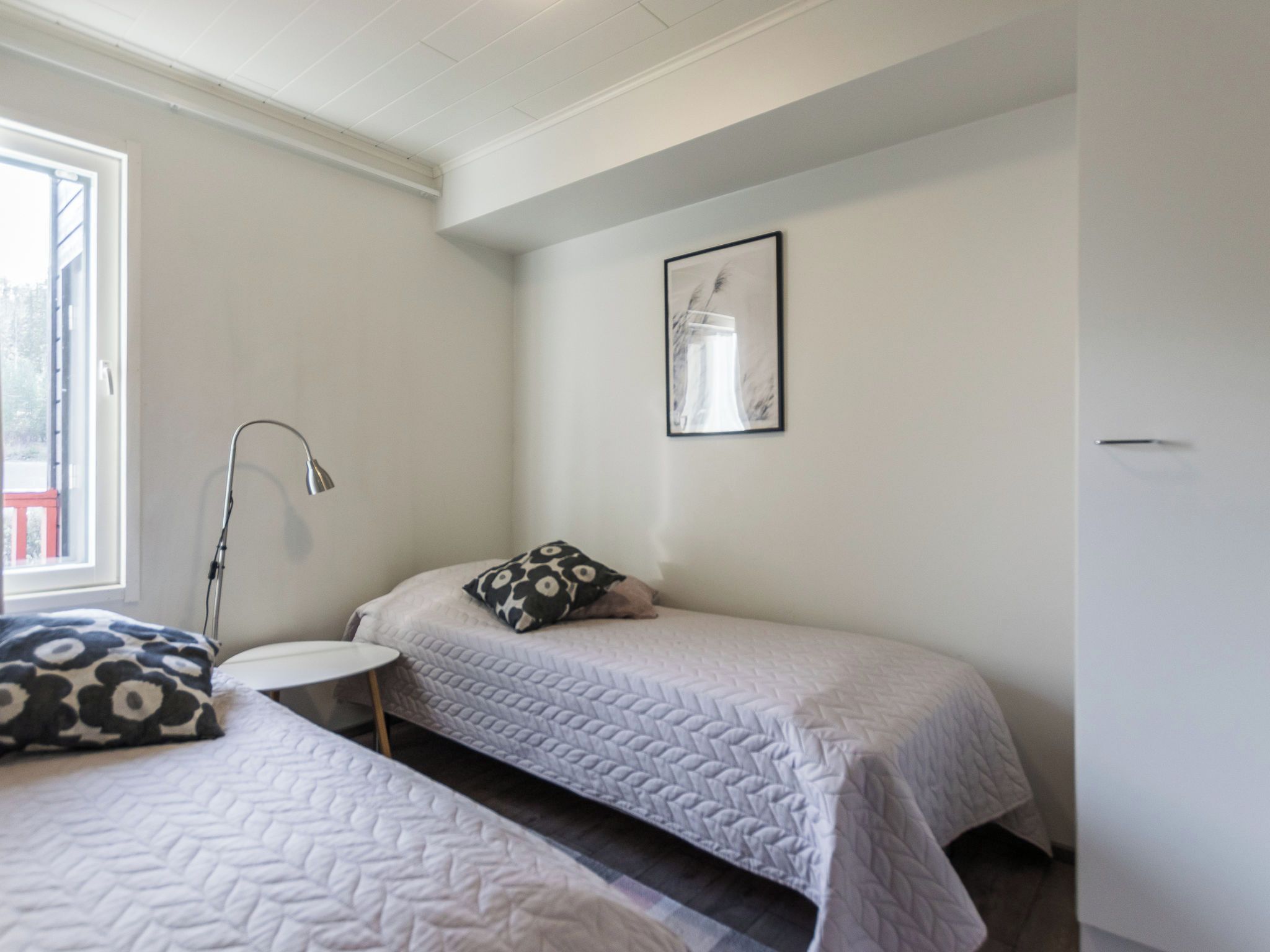 Habitación sencilla y limpia con dos camas, una mesita redonda pequeña y una lámpara de pared individual.