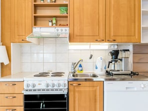 Una cocina con armarios de madera, estufa, pileta y cafetera.