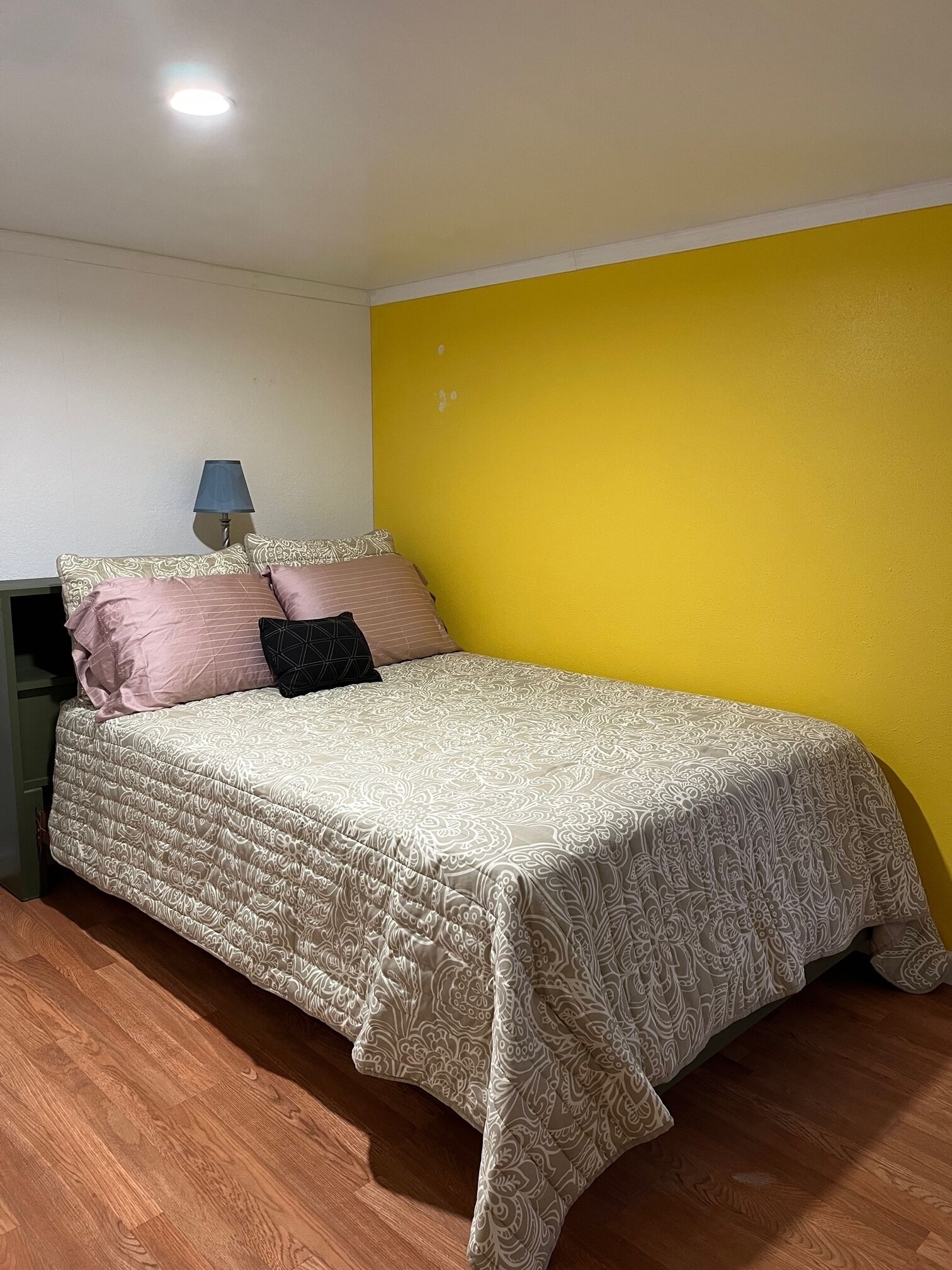Un dormitorio con cama, mesita de noche, lámpara y pared amarilla.
