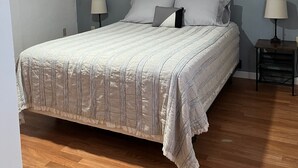 Un dormitorio con una cama grande, dos mesitas de noche con lámparas, un cuadro en la pared y suelo de madera.