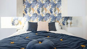 A bedroom with a bed, pillows, a headboard with a tropical leaf pattern, bedside tables, and a window. - Modern 2-Br Apartment in the Heart of Cannes (Cannes)
