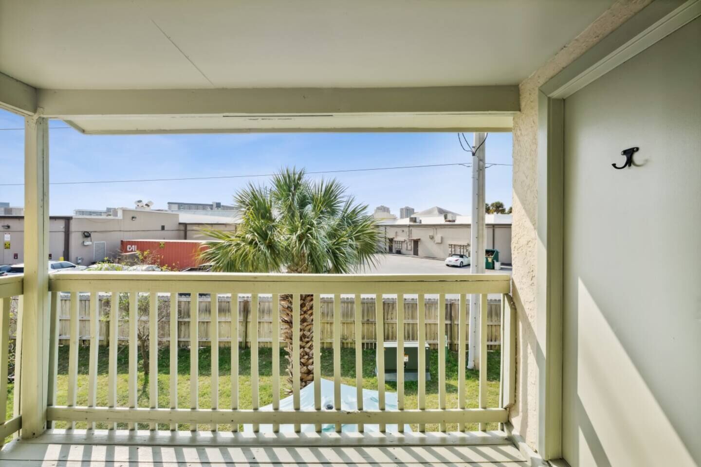 Ein Balkon mit weißer Brüstung, einer Palme und Blick auf Gebäude im Hintergrund.