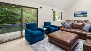 Un salon spacieux doté d’une grande fenêtre, d’un canapé en cuir marron, de fauteuils bleus et d’un coin repas avec des chaises en bois.