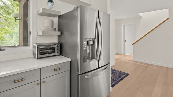 Una cuina moderna amb un frigorífic d'acer inoxidable, un forn tostador integrat i una finestra amb vista a arbres.