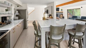 Una cuina moderna amb una illa central, tamborets de bar i un refrigerador de vi integrat.