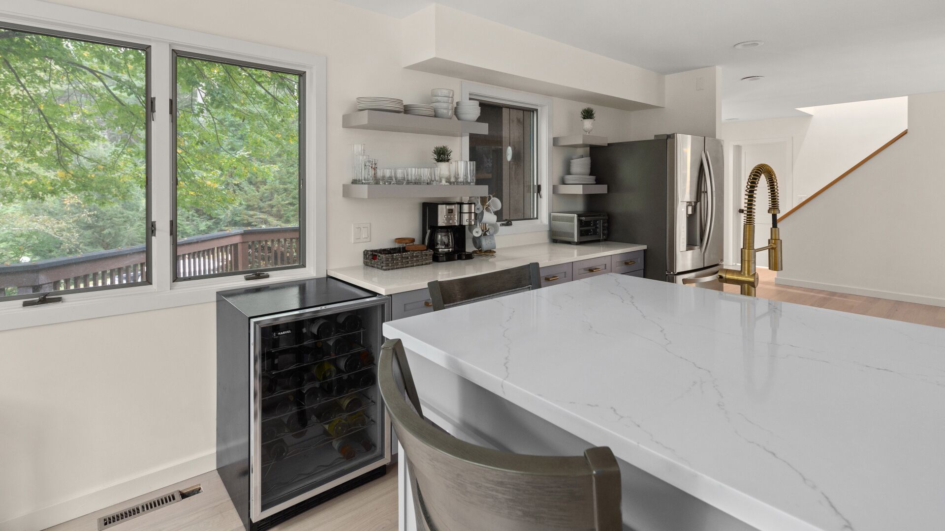A modern kitchen with a large island, built-in appliances, and a view of trees through the windows.