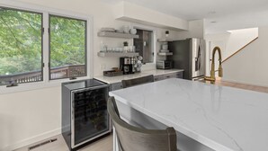 Une cuisine moderne dotée d’un grand îlot central, d’appareils électroménagers intégrés et offrant une vue sur les arbres à travers les fenêtres.