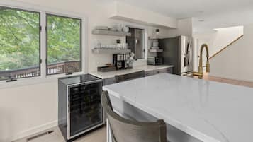 A modern kitchen with a large island, built-in appliances, and a view of trees through the windows.