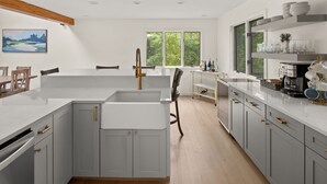 Une cuisine moderne avec des meubles de couleur grise, un îlot central doté d’un évier et une fenêtre donnant sur un espace verdoyant.