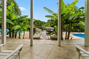 Ein Poolbereich mit einer Anlegestelle, die zu einem kleinen Gebäude führt, umgeben von großen Bananenstauden und blauem Himmel.