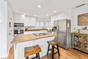 Eine moderne Küche mit weißen Schränken, einem Edelstahl-Kühlschrank und einer Holztresle mit Barhocker.