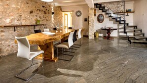 A spacious dining area with a long wooden table, white chairs, and a stone wall. A staircase with a modern design is visible in the background. - Le Muse by Interhome (Castellammare del Golfo)