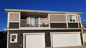 A two-story residential building with a balcony, two garages, and a clear blue sky. - Grey Havens Laneway home w/ garage, balcony, AC near WEM! (Edmonton)