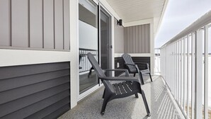 A balcony with two lounge chairs, a sliding glass door, and a white ceiling. - Grey Havens Laneway home w/ garage, balcony, AC near WEM! (Edmonton)
