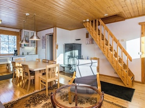 A wooden interior with a dining area, kitchen, and a wooden staircase.