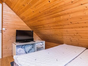 A small, cozy room with a sloped ceiling, a bed, a television on a stand, and a wardrobe.