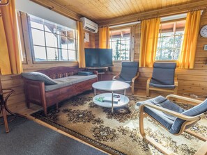 Een gezellig interieur van een blokhut met een bank, twee fauteuils, een salontafel en een televisie.