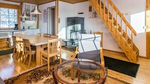 A spacious living area with a wooden staircase, a dining table, and a kitchen area.