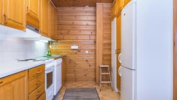 A compact kitchen with wooden cabinets, a white countertop, a built-in oven, a refrigerator, and a small stool.