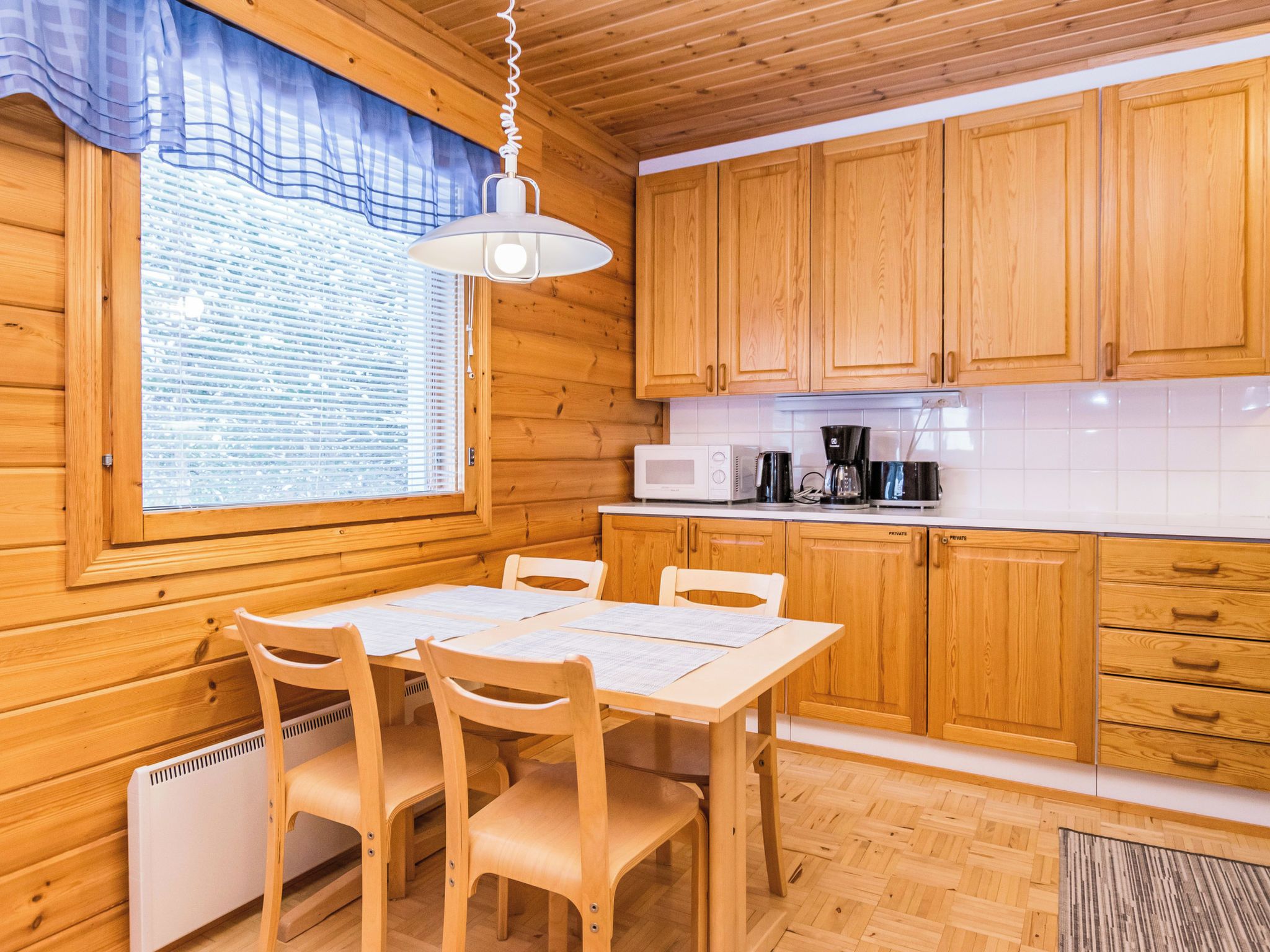 A wooden interior with a dining table, chairs, a window with blinds, wooden cabinets, and a microwave.