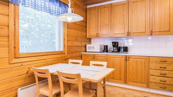 A wooden interior with a dining table, chairs, a window with blinds, wooden cabinets, and a microwave.