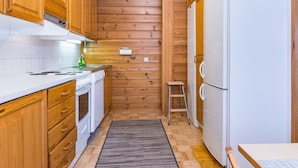 A compact kitchen with wooden walls, white appliances, and a small stool.