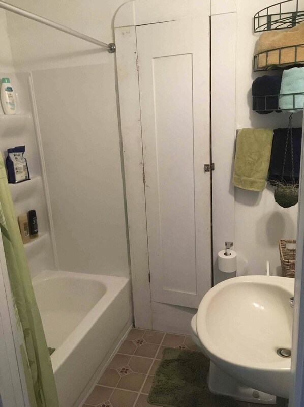 A bathroom with a bathtub, a sink, and a toilet. There are towels hanging on the wall and a shower curtain.