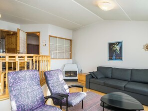 Un salon comprenant un canapé, deux fauteuils à motifs, une petite table, une cheminée et un escalier en bois menant à une autre pièce.