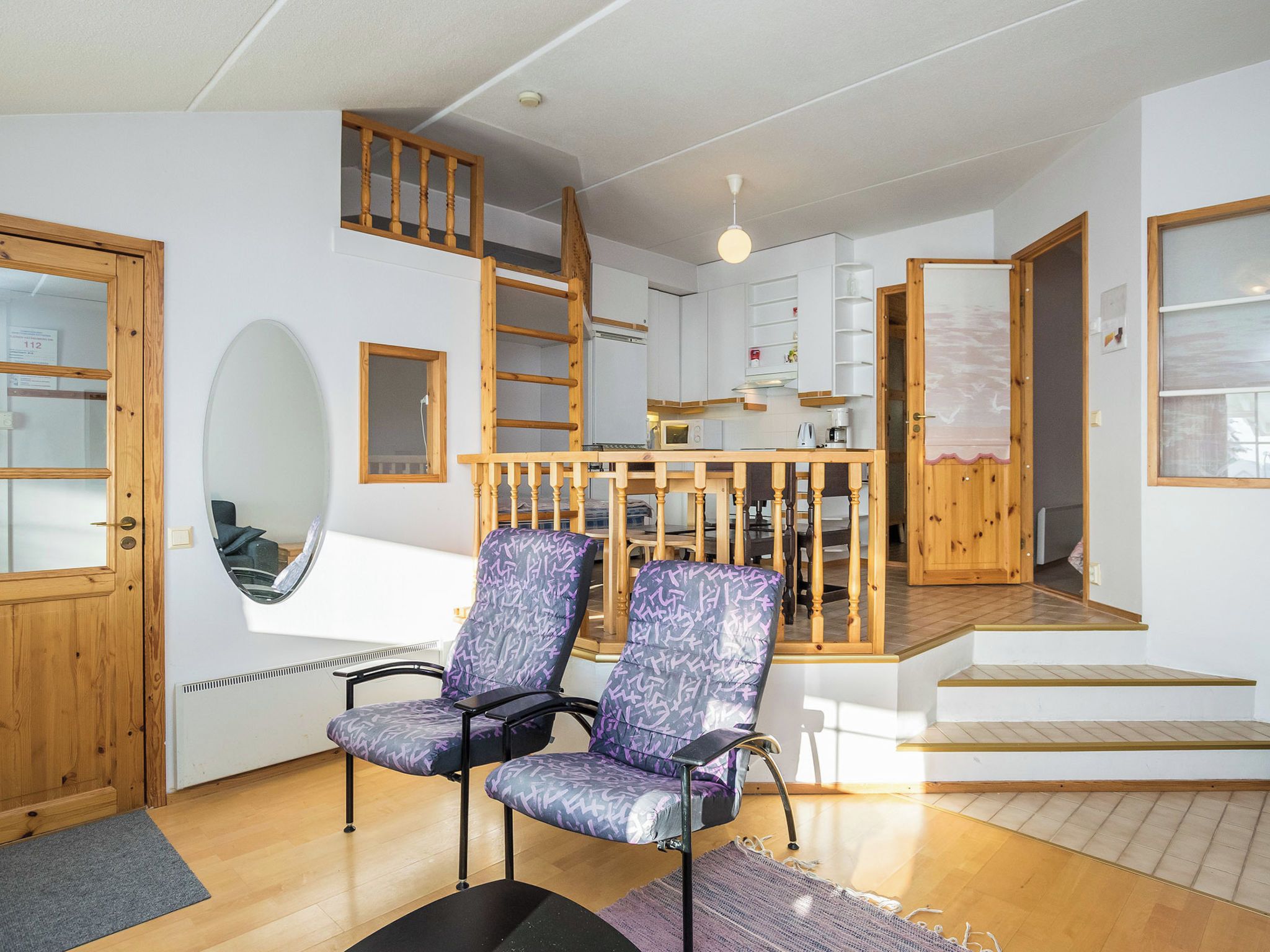 A spacious living area with a staircase leading to a loft, a dining table, and two patterned chairs.