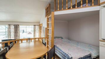 A bunk bed room with a wooden table and chairs, a window with curtains, and a white appliance.