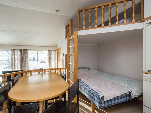Une chambre avec un lit superposé, une table et des chaises en bois, une fenêtre avec des rideaux et un appareil électroménager blanc.
