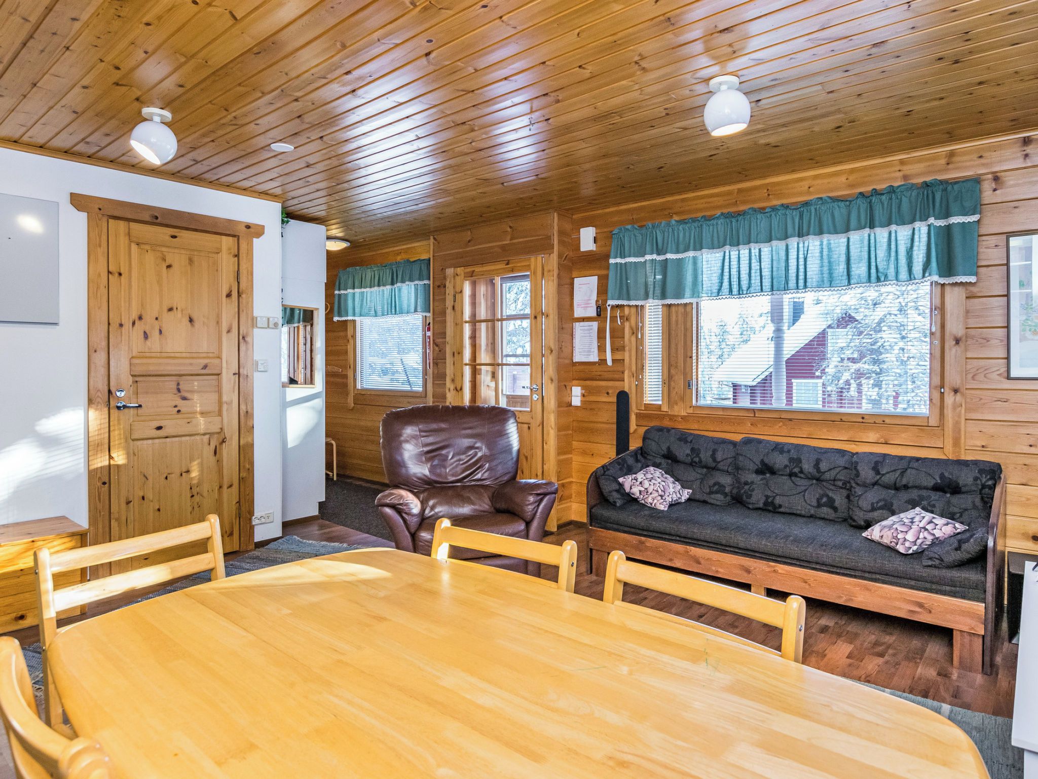 Interior de uma cabana de madeira com uma mesa de jantar, cadeiras, um sofá de couro e teto de madeira.