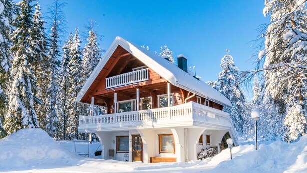 A two-story wooden cabin with a balcony, surrounded by snow-covered trees. - Kulma-alpit a by Interhome (Hyrynsalmi)