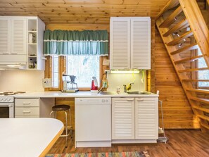 Une cuisine avec des murs en bois, une fenêtre avec des rideaux, une cuisinière, un évier et un lave-vaisselle.