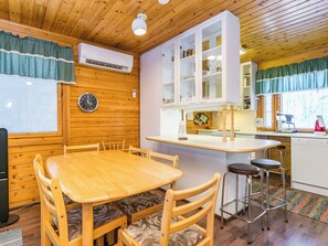 Ein Holzinterieur mit einem Esstisch, Stühlen, einer Küchenzeile mit Schränken und einer Uhr an der Wand.