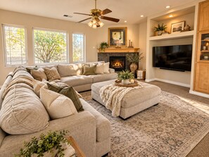 A living room with a sectional sofa, a fireplace, a television, and a ceiling fan.