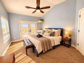 A bedroom with a bed, a bench, a nightstand, a ceiling fan, and a view through the door.