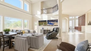 A spacious living room with a high ceiling, a dining area, and a view of the outdoors.