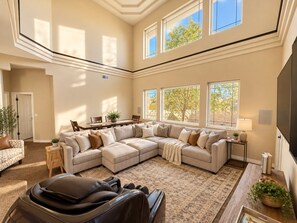 A spacious living room with a large sectional sofa, a massage chair, and a dining area with a table and chairs.