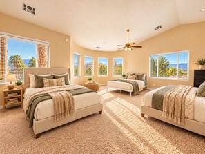 A bedroom with two beds, a ceiling fan, and large windows with a view.