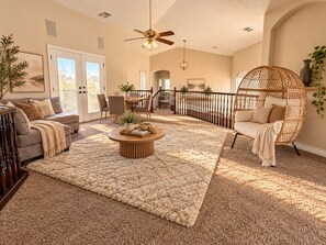 A spacious living room with a large round coffee table, a comfortable sofa, a wicker swing chair, and a dining area with a wooden table and chairs.