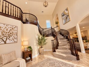 A spacious living area with a curved staircase, a fireplace, and a large abstract painting.