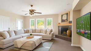 A living room with a sectional sofa, a fireplace, and a large TV screen displaying a sports game.