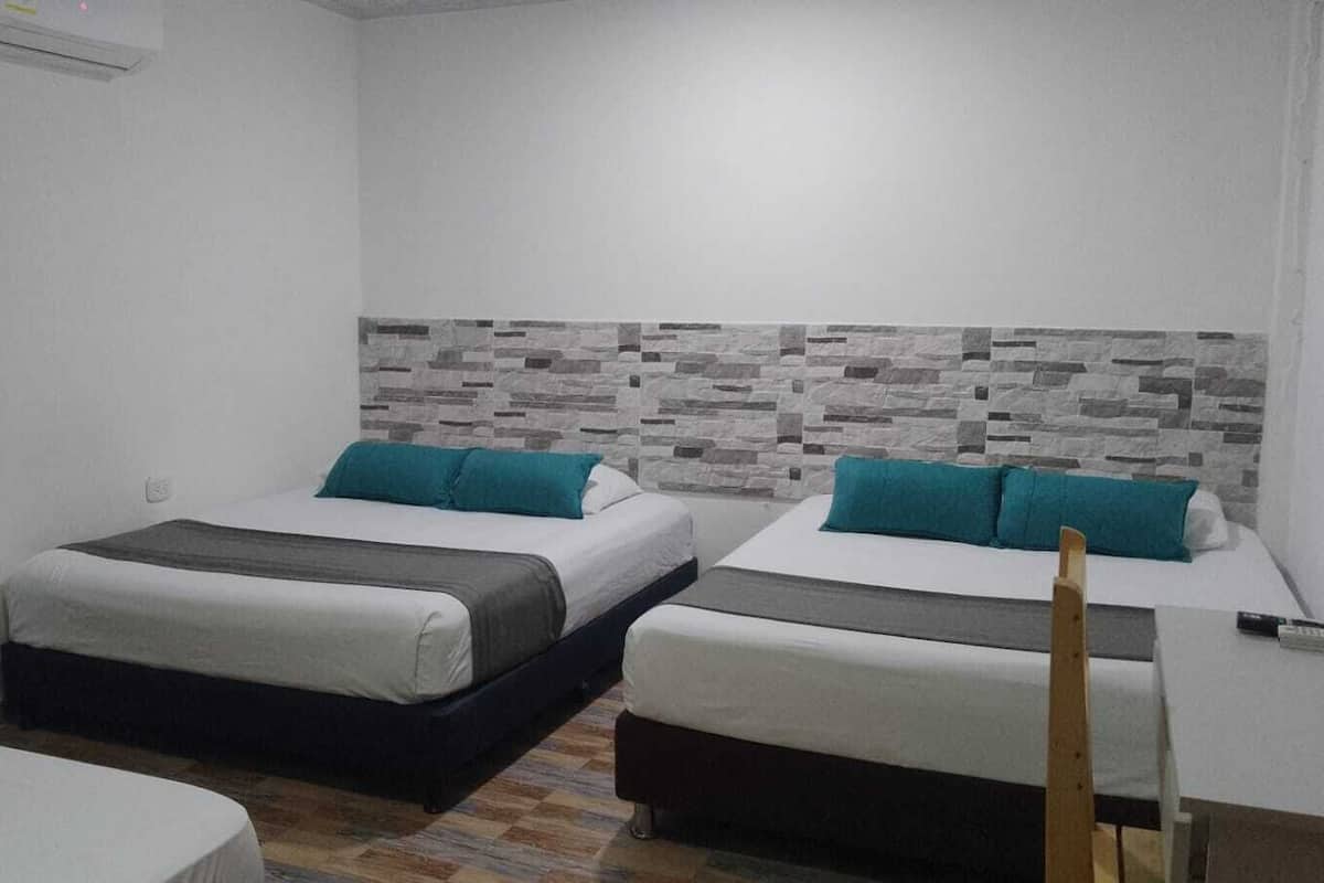 Ein kleines, sauberes Zimmer mit zwei Betten, einer Wand mit Fliesen und einem Holzstuhl.