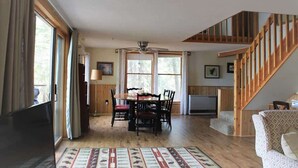 Un vaste espace de vie comprenant une table à manger, des chaises, un canapé, un escalier et de grandes fenêtres.